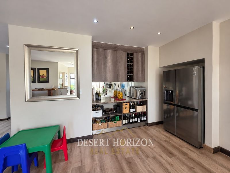 A modern kitchen area featuring built-in cabinetry, a dedicated wine rack, stone countertops, and recessed lighting, complemented by durable laminate flooring.
