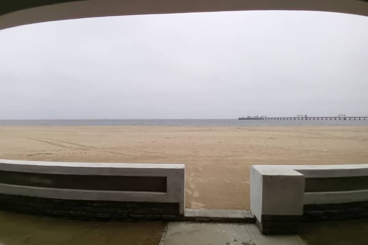 Direct beach access view featuring a low masonry boundary wall and a paved path leading toward the sandy shoreline and ocean.