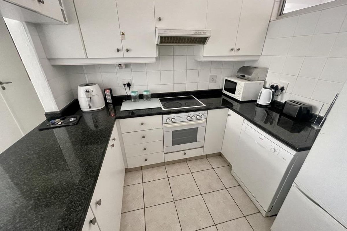 Compact kitchen featuring white cabinetry, dark granite countertops, built-in oven, electric hob, extractor fan, and tiled flooring.