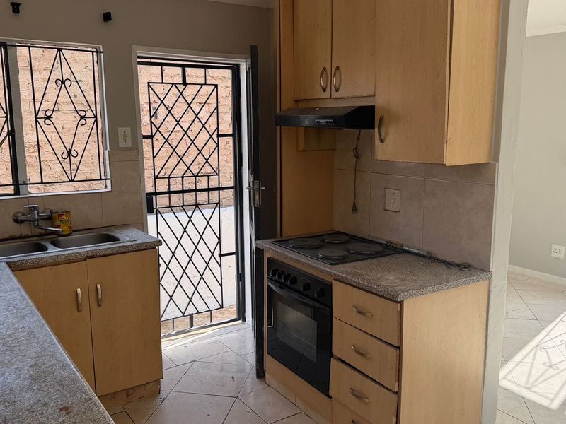 Functional kitchen featuring built-in cabinetry, electric oven and hob, double sink, and direct access to the exterior via a security gate.