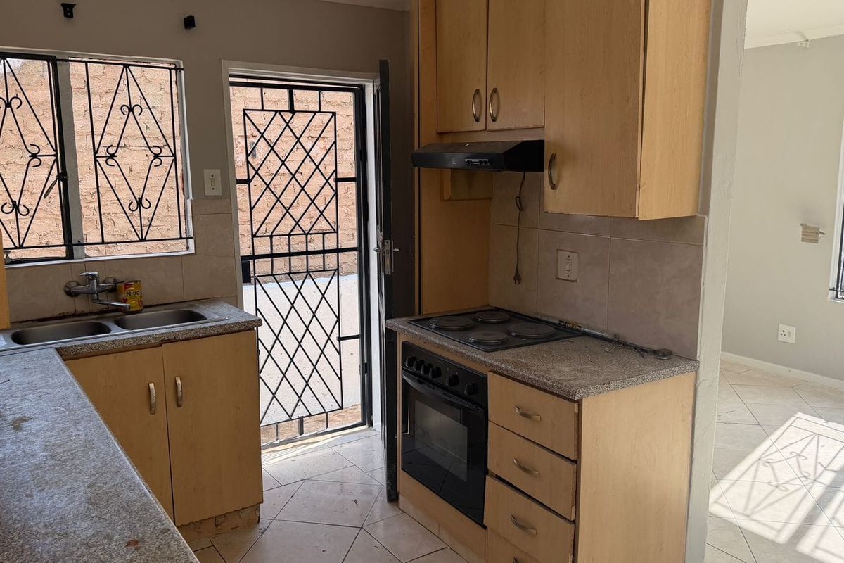 Functional kitchen featuring built-in cabinetry, electric oven and hob, double sink, and direct access to the exterior via a security gate.