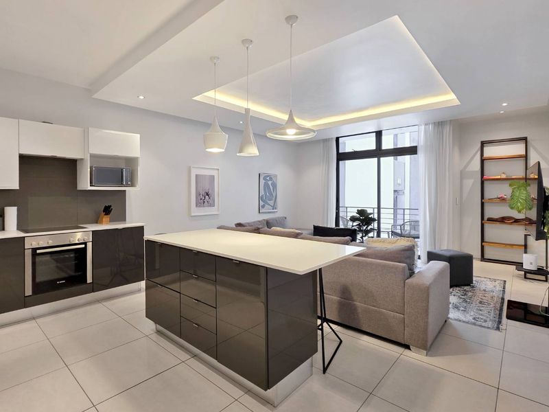 Modern open-plan living area featuring a sleek kitchen with a central island, built-in appliances, and recessed ceiling lighting, flowing into a bright lounge space.