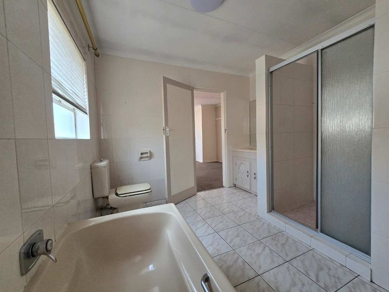 A dated bathroom featuring a built-in bathtub, separate shower enclosure, vanity cabinet, and toilet, with neutral wall and floor tiling throughout.