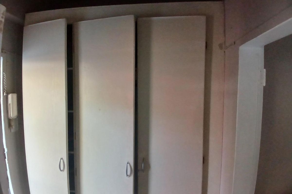 A bedroom featuring built-in cupboards and an intercom system, showing signs of wear and requiring cosmetic updates.
