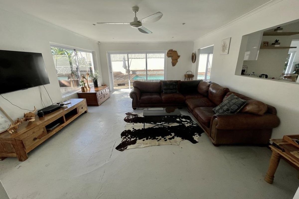 Spacious living room featuring a ceiling fan, painted concrete flooring, and sliding glass doors providing direct access to the outdoor pool area.