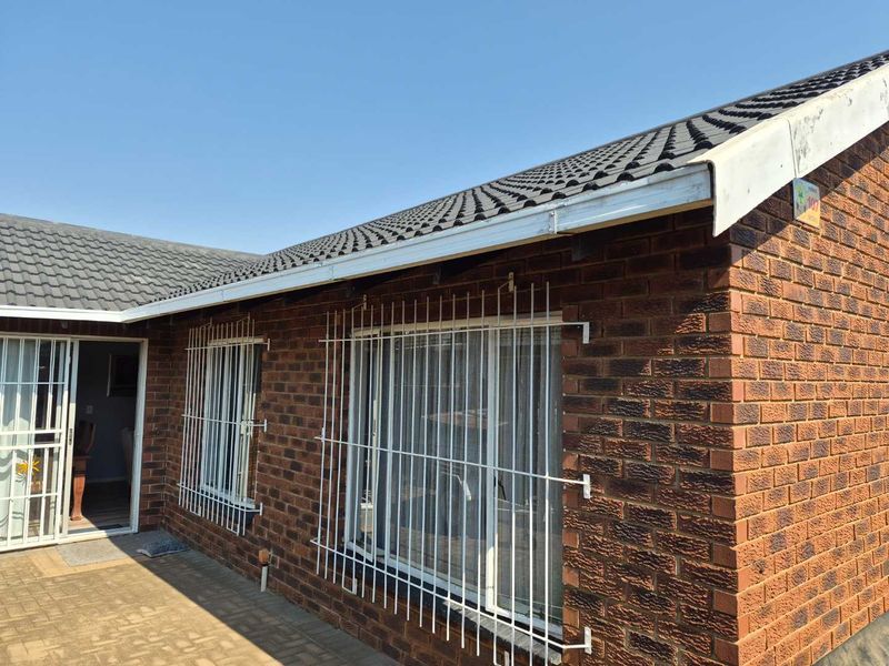 Rear exterior view of a face brick townhouse featuring a tiled roof, security bars on windows, and a paved patio area.
