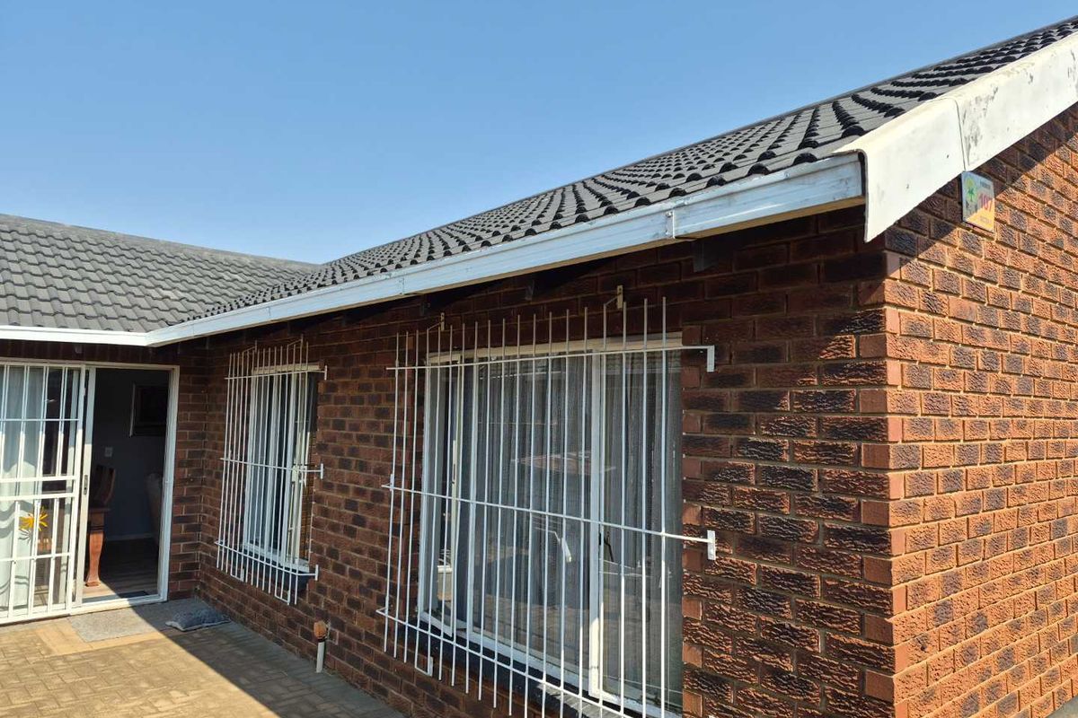 Rear exterior view of a face brick townhouse featuring a tiled roof, security bars on windows, and a paved patio area.