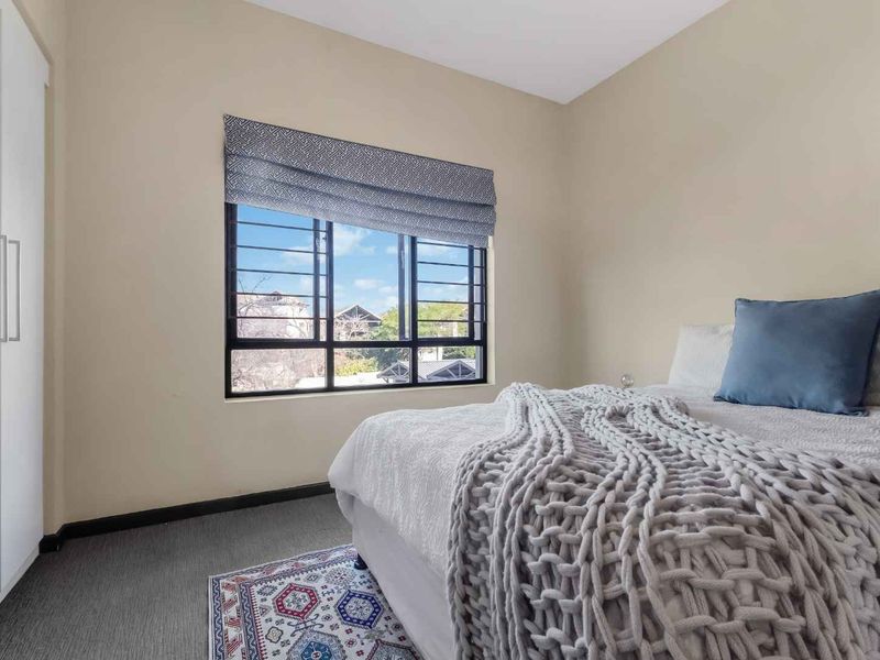 A well-maintained bedroom featuring neutral walls, carpeted flooring, a built-in wardrobe, and a window fitted with security bars.