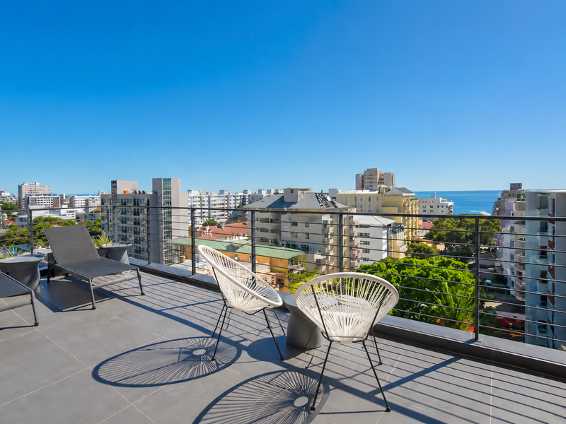 Spacious balcony featuring modern tiled flooring and a sleek metal railing, offering expansive urban and coastal views.
