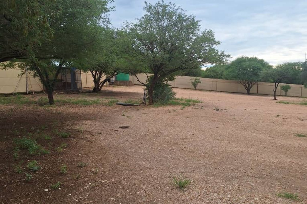 A spacious, open industrial rear yard area featuring gravel ground cover, perimeter fencing, and a partial shade sail structure.