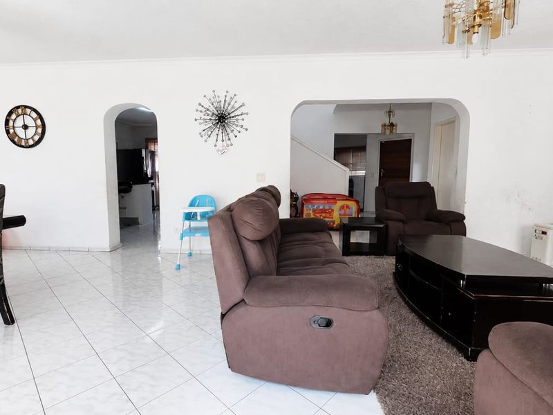 Spacious open-plan living and dining area featuring tiled flooring, arched architectural transitions, and a staircase leading to the upper level.