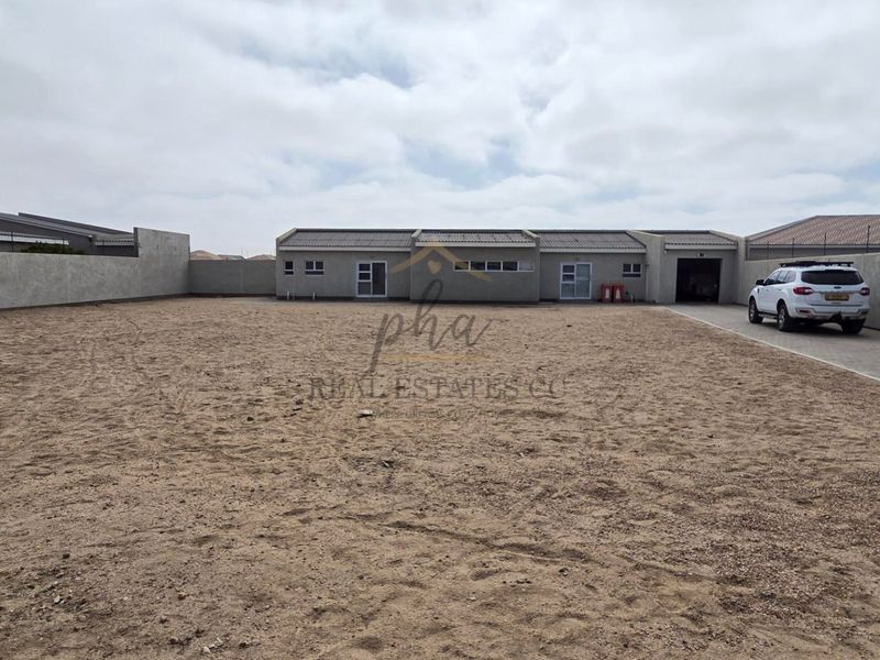 A rear view of the property featuring a large, unlandscaped yard, perimeter boundary walls, and a paved driveway leading to the garage.