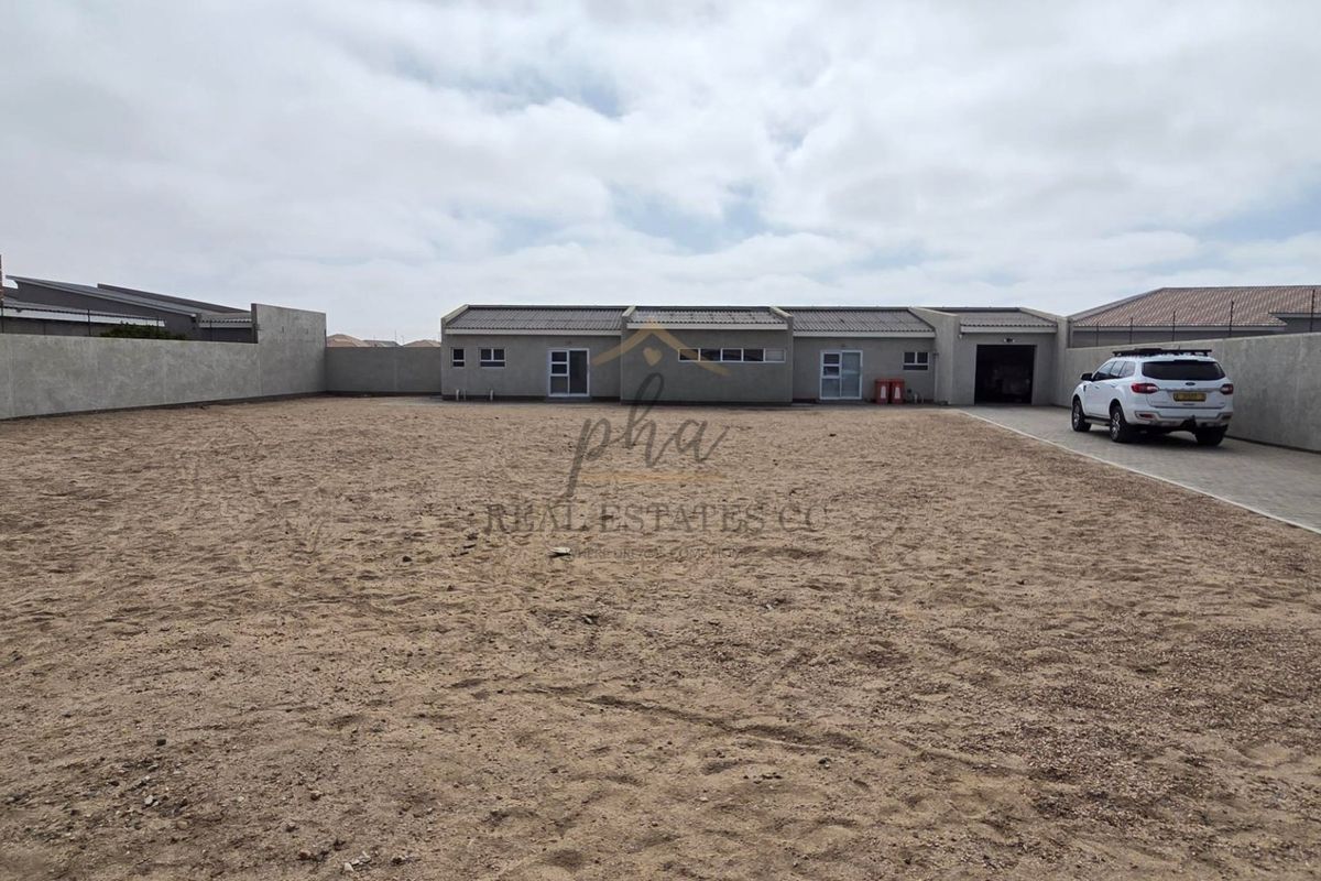 A rear view of the property featuring a large, unlandscaped yard, perimeter boundary walls, and a paved driveway leading to the garage.