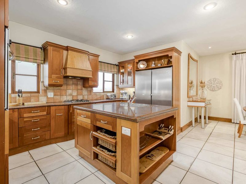 A well-maintained kitchen featuring wooden cabinetry, granite countertops, a central island, and tiled flooring, offering a functional and classic cooking space.