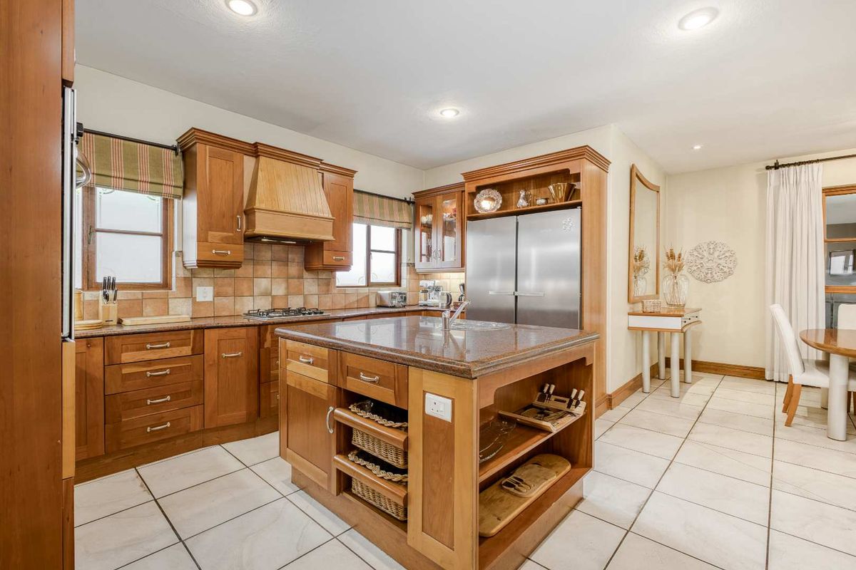 A well-maintained kitchen featuring wooden cabinetry, granite countertops, a central island, and tiled flooring, offering a functional and classic cooking space.