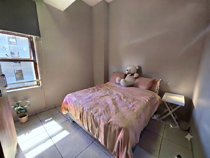 A compact bedroom featuring tiled flooring and a window with a roller blind, providing natural light and a functional living space.