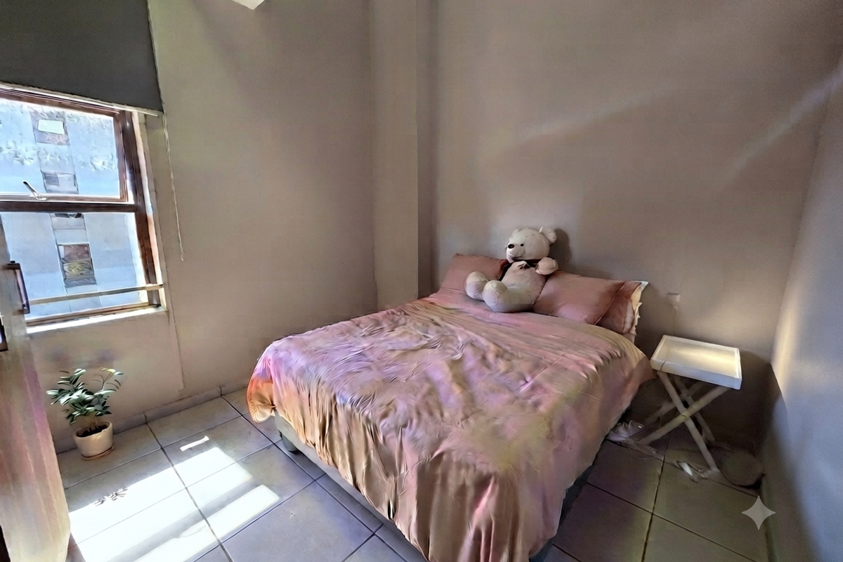 A compact bedroom featuring tiled flooring and a window with a roller blind, providing natural light and a functional living space.