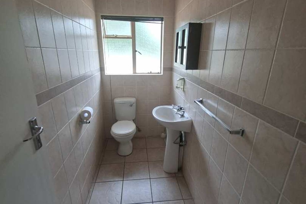 A compact bathroom featuring full-height wall tiling, a pedestal basin, and a standard toilet, providing a functional and clean utility space.
