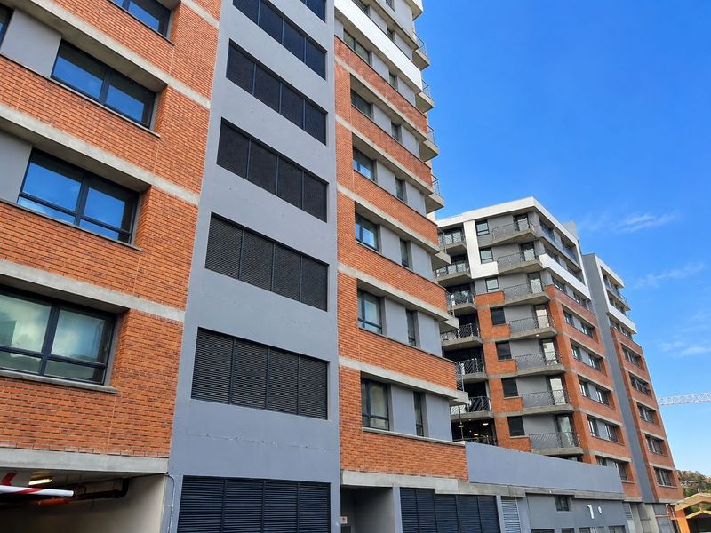 Modern multi-story apartment complex featuring a contemporary brick and grey facade with integrated balconies and security shutters.