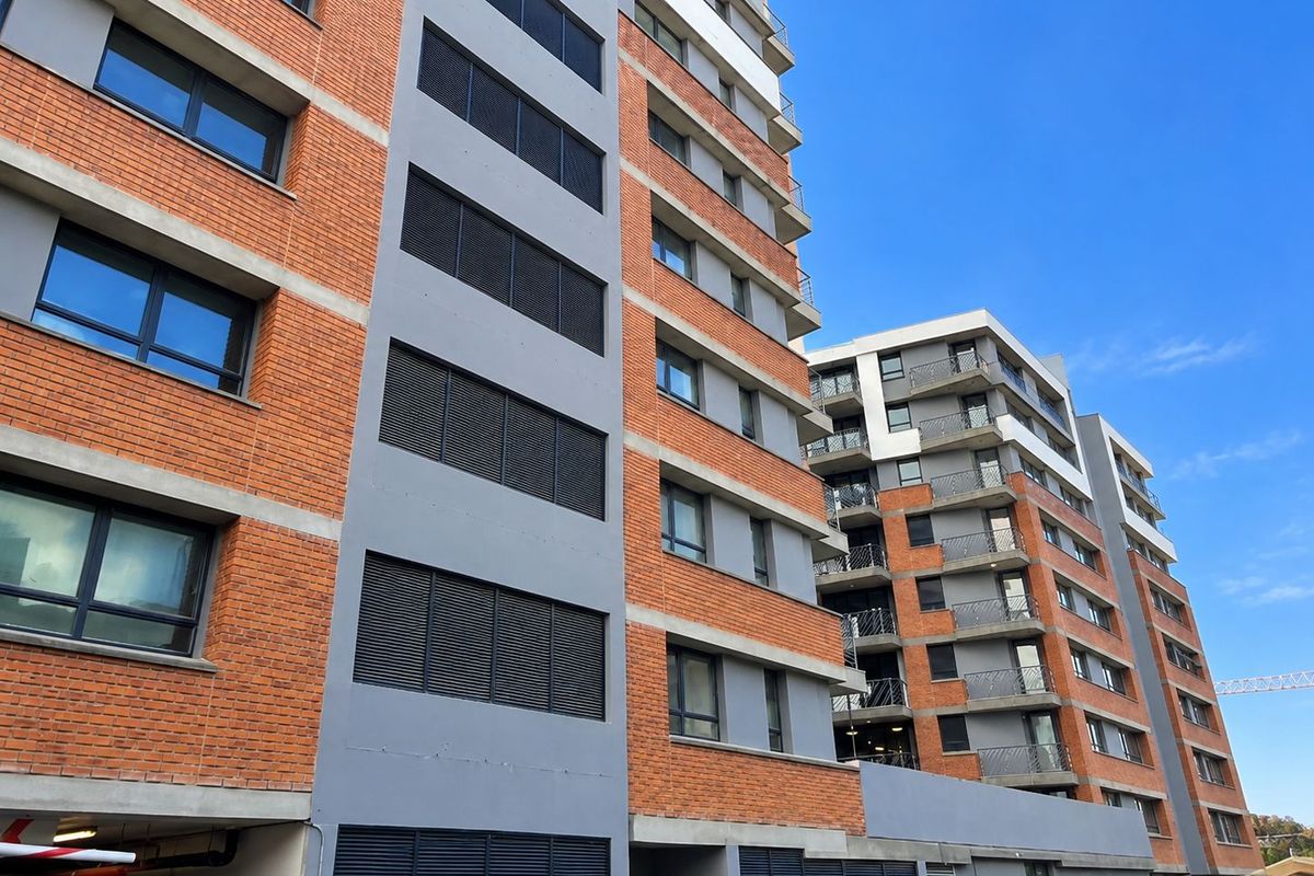 Modern multi-story apartment complex featuring a contemporary brick and grey facade with integrated balconies and security shutters.
