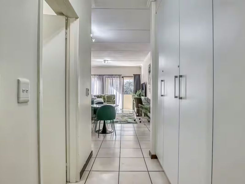 A bright hallway featuring tiled flooring and ample built-in cupboard storage, leading directly into the open-plan living area.