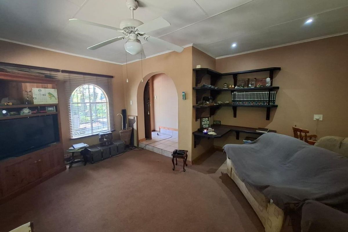 A living room featuring an arched doorway, built-in shelving, a desk area, and an arched window with venetian blinds.