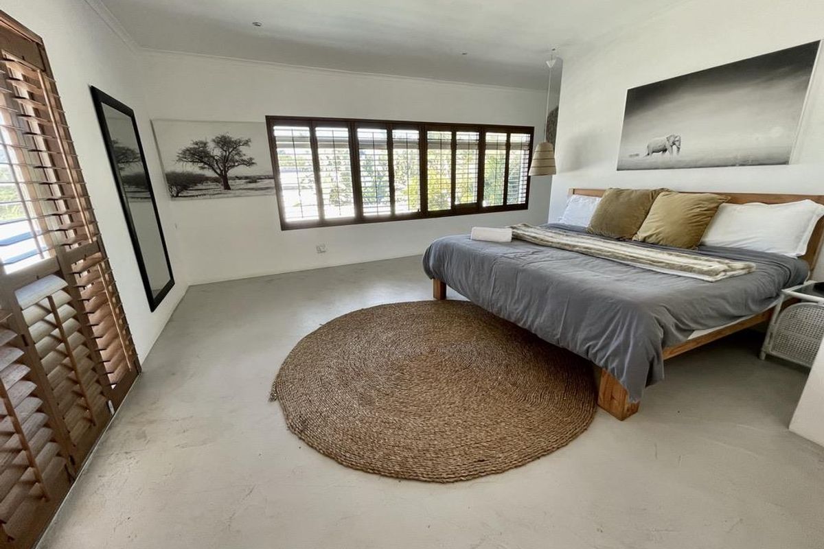 Spacious bedroom featuring polished concrete floors, large timber plantation shutters, and recessed lighting, creating a bright and airy atmosphere.