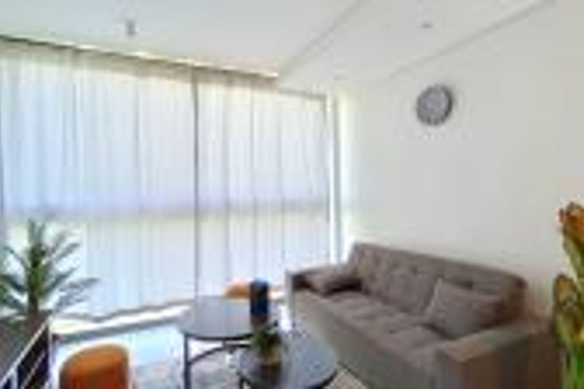 A bright and modern living room featuring large floor-to-ceiling windows with sheer curtains, providing ample natural light and a clean, neutral aesthetic.