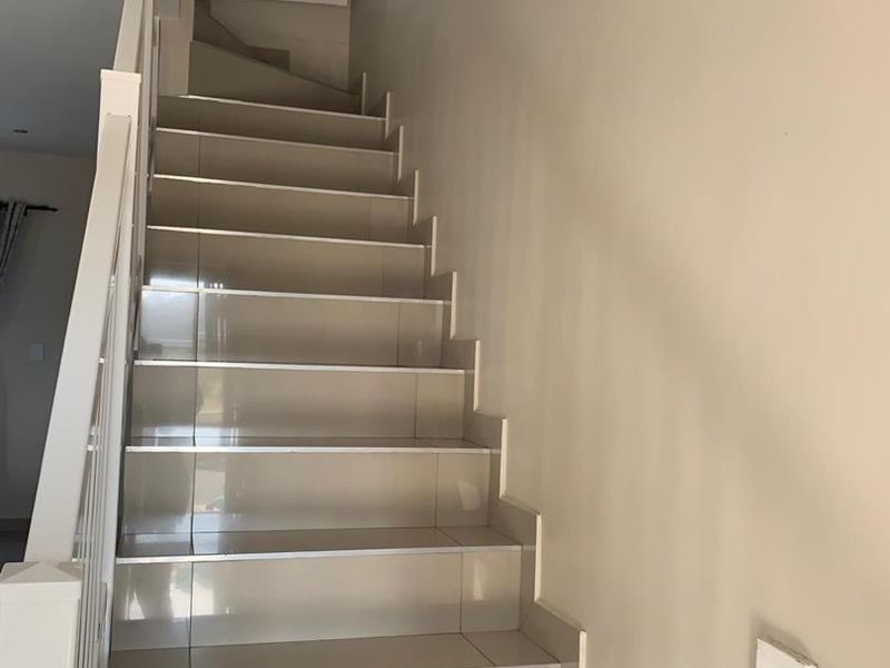 A clean, tiled staircase featuring a white balustrade and handrail, providing access to the upper level of the townhouse.