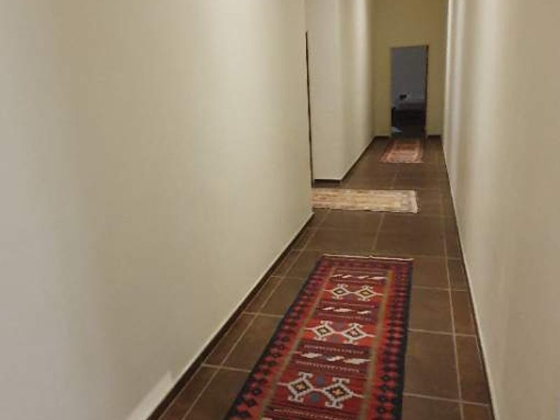 A long, neutral-toned hallway featuring tiled flooring and recessed downlighting, providing a clean and simple transition between rooms.