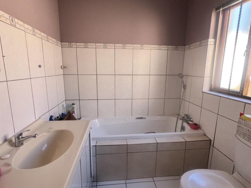 A dated bathroom featuring a built-in vanity, bathtub with shower mixer, and toilet, finished with neutral wall and floor tiles.