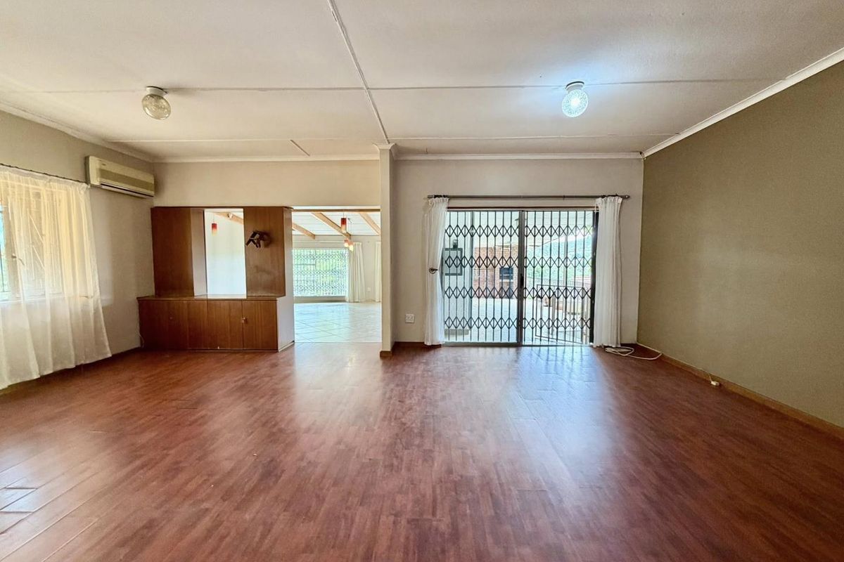 Spacious living area featuring wood-look flooring, built-in cabinetry, wall-mounted air conditioning unit, and sliding glass doors with security gate leading to the exterior.