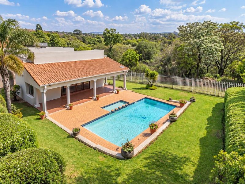 Aerial view of the rear exterior featuring a swimming pool, covered patio, and well-maintained garden set against a scenic landscape.