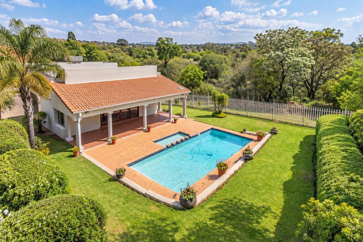 Aerial view of the rear exterior featuring a swimming pool, covered patio, and well-maintained garden set against a scenic landscape.
