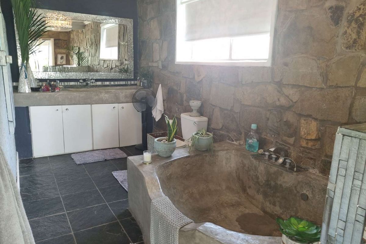 A rustic-style bathroom featuring a custom concrete bathtub, stone feature wall, slate floor tiles, and a built-in vanity with a large mirror.