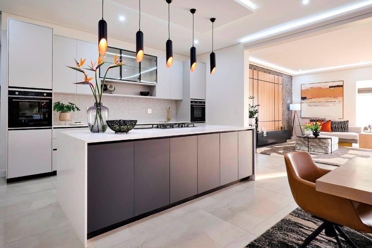 Modern open-plan kitchen featuring a large central island, sleek cabinetry, built-in appliances, and stylish pendant lighting, seamlessly flowing into the living area.