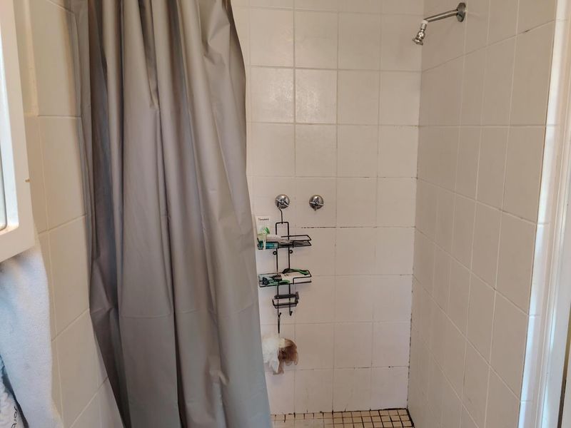 A functional shower enclosure featuring white wall tiles, a tiled floor, and a standard shower head fixture.