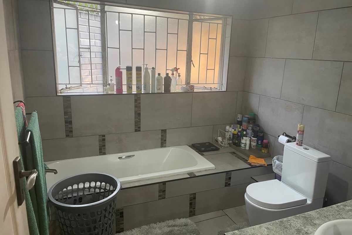 A functional bathroom featuring a built-in bathtub, tiled wall finishes, and a standard toilet, with security bars installed on the window.