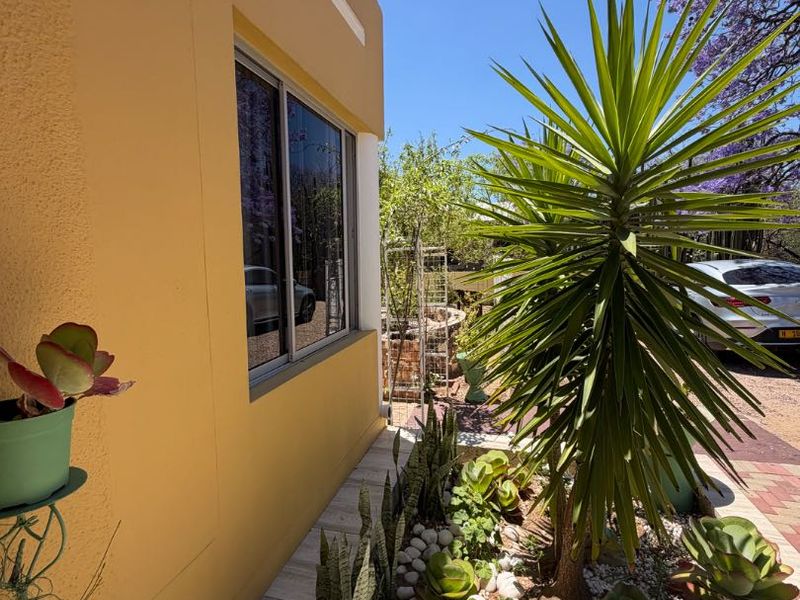 A well-maintained front exterior view featuring a yellow facade, modern aluminium window frames, and a landscaped garden bed with pebble accents.