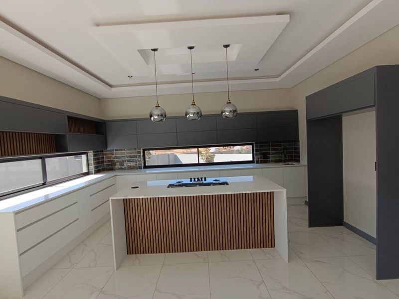 Modern kitchen featuring a central island with timber detailing, sleek handleless cabinetry, stone countertops, and high-end integrated hob, set against a tiled backsplash.