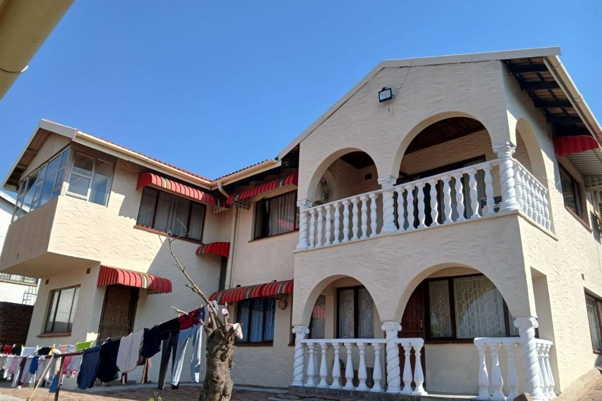 Rear view of a two-story house featuring a double-level arched balcony with balustrades, paved patio area, and striped window awnings.