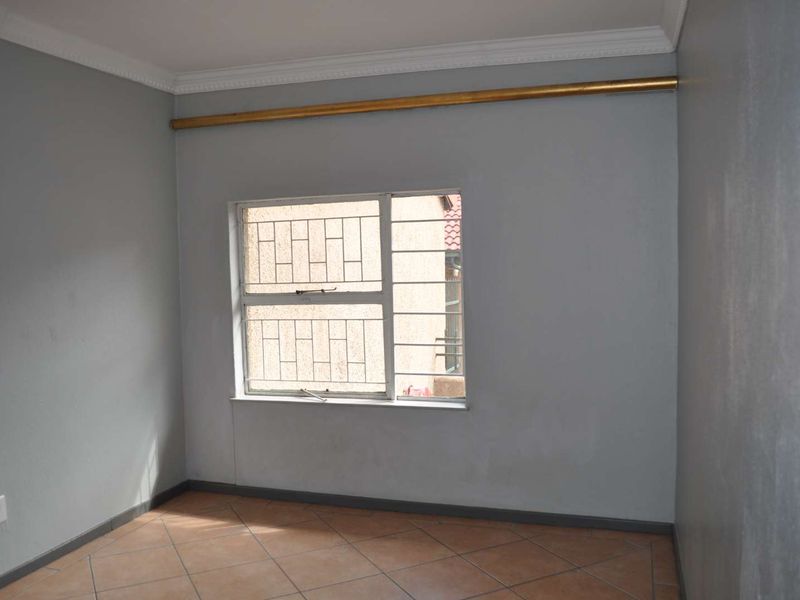 An empty bedroom featuring tiled flooring, security bars on the window, and neutral grey walls, providing a blank canvas for personalization.
