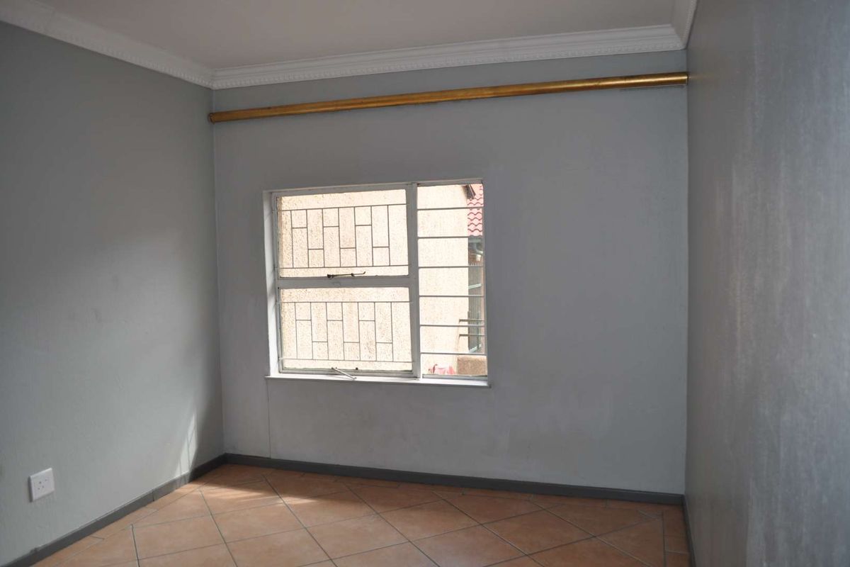 An empty bedroom featuring tiled flooring, security bars on the window, and neutral grey walls, providing a blank canvas for personalization.