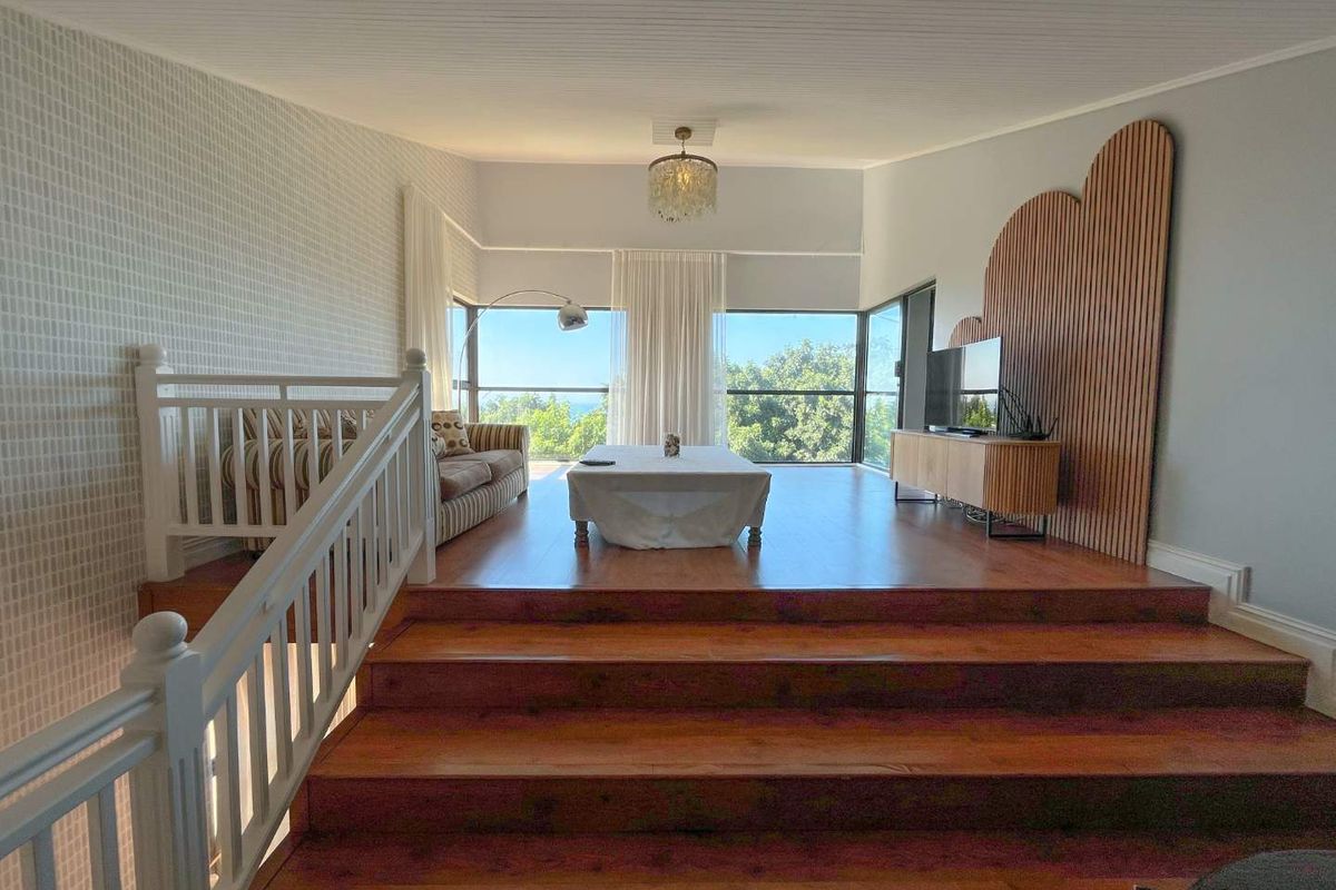 Spacious elevated living area featuring timber flooring, decorative wall paneling, and large windows offering scenic views.