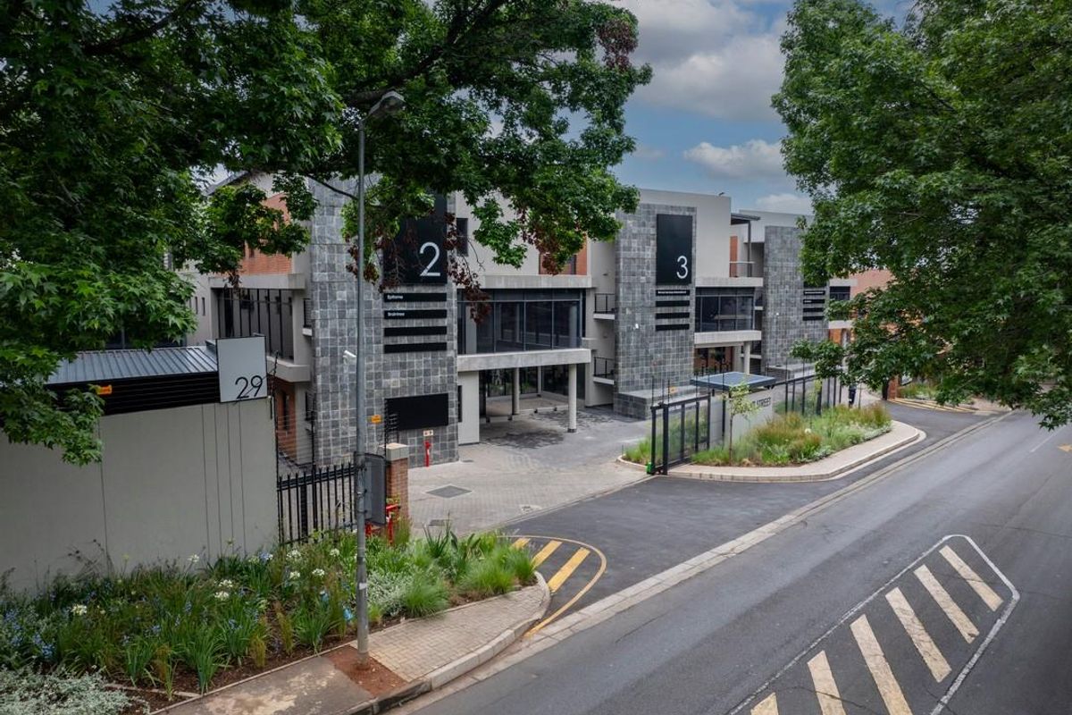 Modern office complex exterior featuring stone cladding, glass facade, and secure gated entrance with paved driveway access.