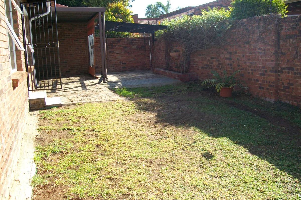 A private rear garden featuring a paved patio area, a metal pergola, and a brick boundary wall, offering potential for landscaping and outdoor living.