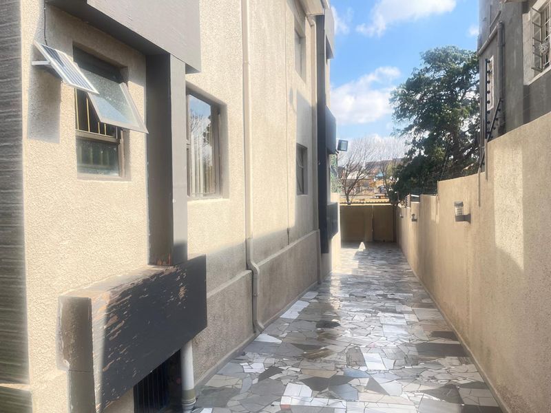A narrow side passage featuring crazy paving flooring, boundary walls with security spikes, and exterior wall-mounted lighting.