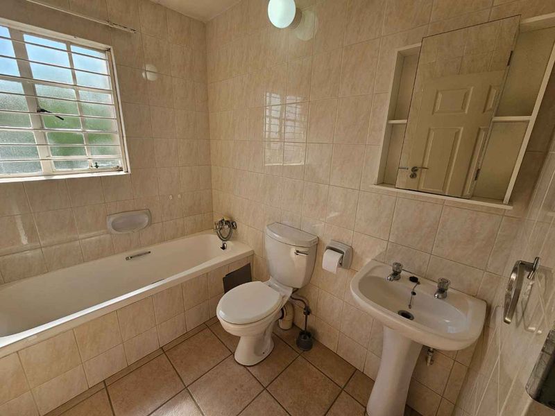 A functional bathroom featuring a bathtub, pedestal sink, toilet, and tiled finishes throughout, offering a clean and practical space.