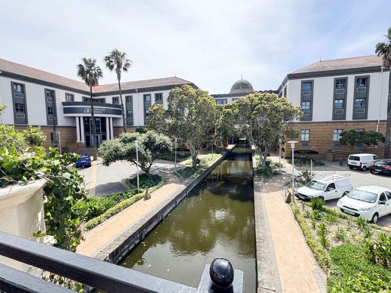 Exterior view of a professional office complex featuring a central canal, landscaped gardens, and paved walkways between multi-story buildings.