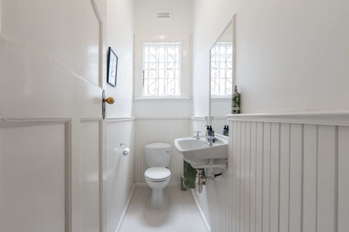 A compact powder room featuring classic wainscoting, a wall-mounted basin, and a window with a security grille.